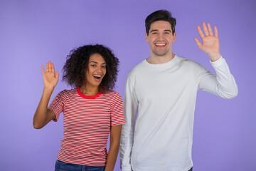 Interracial friendly couple - white man and african woman waving hands - hello. Greeting, say Hi to camera on purple studio background. © kohanova1991