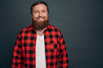 Waist-up shot pleasant, friendly young attractive bearded guy in red checkered shirt,talking casually with friends at party, smiling satisfied, showing happy positive emotion, standing grey background