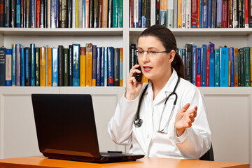 Telehealth concept: doctor in front of a computer and talking on the phone with a patient.
