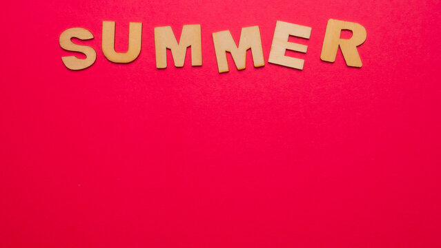 Wooden letters with the word "summer" horizontally in the upper margin of the image on a pink background
