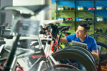 Handsome young bicycle store owner with digital tablet checking vehicles he received for selling