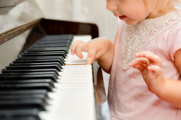 A little girl presses her fingers on the white keys of the piano. Teaching children at a music school.