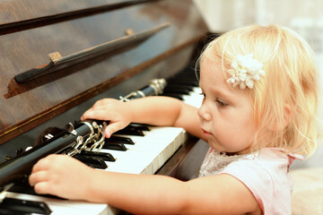 The little girl takes the clarinet lying on the black piano keys.