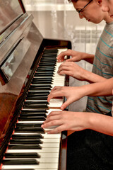 Fototapeta premium A girl and a guy play the piano in four hands. Rehearsal and training at a music school.