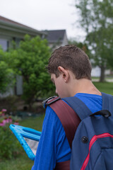 Boy with Autism waiting for the school bus; child wears bus harness and backpack he's turned away from the camera 