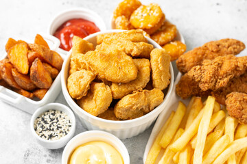 Chicken nuggets, strips, french fries, fried potatoes, ketchup and cheese sauce on a light background. Fast food closeup	
