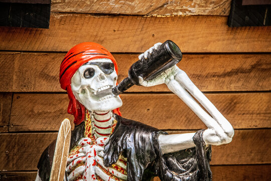 Grungy painted and glued together bloody skeleton pirate drinking beer with boat hull background Halloween decoration - closeup