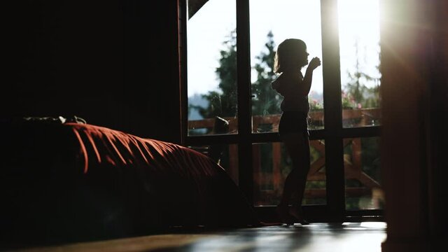 Funny girl jumping, dancing at home. Happy female customer excited about success. Silhouette happy carefree young kid girl dancing alone in modern living room with big window