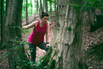 Exhausted young female athlete leaning on a tree deep in a forest. Woman runner catching her breath during outdoor workout.