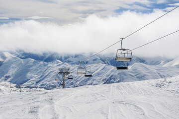 An empty chairlift on the background of snow-covered ridges tightened