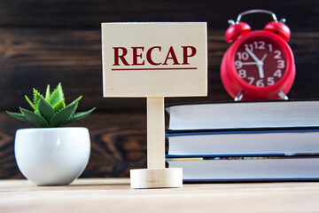 RECAP - a word on a wooden board against the background of books, an alarm clock, a cactus