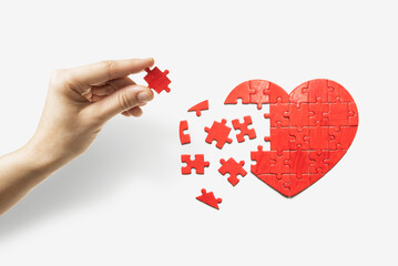 Heart-shaped puzzle and human hand with the missing piece of puzzle. Love relationships concept.