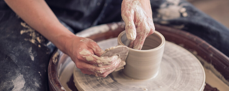 Close up female hands make dishes from clay. woman hands working on potters wheel. The master potter works in a workshop. banner