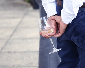 person holding a glass of white wine behind their back with linked hands
