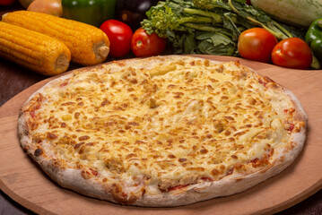 Chicken and mozzarella pizza on a wooden board and vegetables in the background.