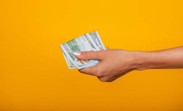 Close up photo of beautiful female hands holding the bunch of dollars of USA isolated on yellow background. Economy, business and finance concept