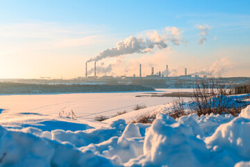 on a cold winter day on the other side of the frozen river a smoking factory
