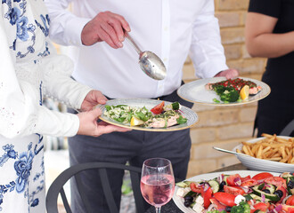 Man serving food to his wife at an outdoor summer buffet