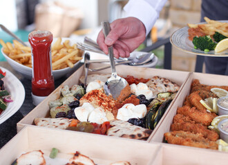 Hand of a man taking food from a buffet table.  Very posh boxed catering at an outdoor garden party
