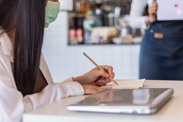 A woman sits alone in a coffee shop with her notes and plans in a notebook, and wears a mask all the time when she hasn't had a cup of coffee. learning concepts and note taking in notebooks