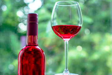 Close-up of a creative summer composition with rose wine and a large glass against a background of greenery. Romantic dinner or breakfast.