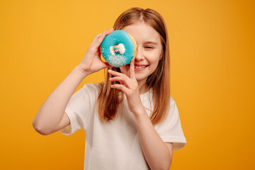 Girl child with sweet blue donut sniling isolated on yellow background with copyspace. Portrait of beautiful teen kid holding doughnut