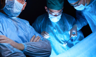 Group of surgeons at work in operating theater toned in blue. Medical team performing operation