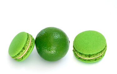 Green macaroon and fresh green lime on white background. High definition photo in close up. Lime macaroon cake isolated. Green dessert with pistachio flavor and green cream. High quality photo