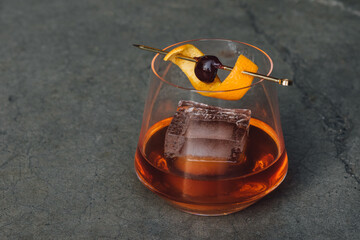 bourbon whiskey old fashioned cocktail with large ice cube and cherry orange on gold cocktail pick 