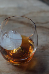 glass dram of whiskey whisky with sphere ice on wood table 