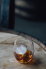 dram of whiskey in a glass with sphere spherical ice on wood barrel 
