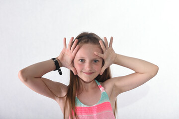 A beautiful school-age girl in the studio on a white background plays scenes with palms and fingers...