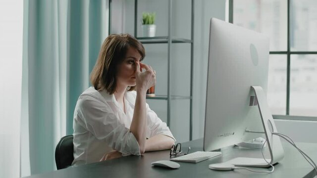 Tired lady boss puts on glasses to work on computer at table