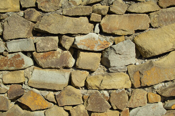 Frontal view of a wall made of brown, yellow, gray treated stones, held together with mortar. .Stones of different shapes and sizes. .Texture, background. .