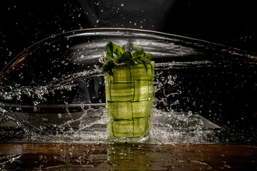 wonderful view of glass braided with green cucumber with splash water drops around it