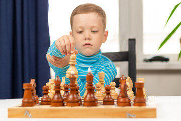 Cute seven year old child boy playing chess at home on a white wooden table. Selective focus....