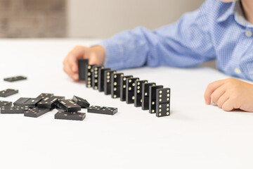 Six year old cute boy plays dominoes at home on a white wooden table. Selective focus. Close-up