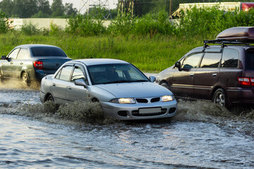 The car is driving through a deep puddle. Splashes are flying from under the wheels of the car. Flood in the city. The consequences of a downpour.
