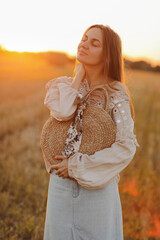 girl with long hair and straw bag in hand in the summer at sunset in the field for a walk. she is happy, her eyes are closed. background blurred art photography