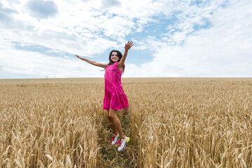 Naklejka na ściany i meble Young beautiful woman in a dress walk on a golden wheat field, summer