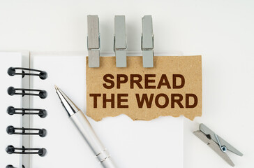 On a white background lies a notebook, a pen, clothespins and cardboard with the inscription - Spread The Word