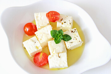 Feta cheese cubes with cherry tomato and olive oil in white bowl
