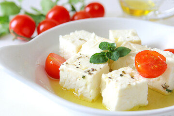 Feta cheese cubes with cherry tomato and olive oil in white bowl