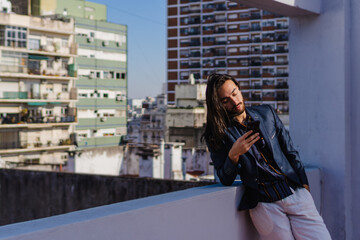 young hispanic latino male long haired businessman leaning on his terrace checking his smart phone. elegant, copy space