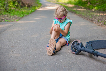The girl fell while riding a scooter in the park and severely injured her knee. Electric scooter injury concept. Panoramic shot with place for text © SERSOLL