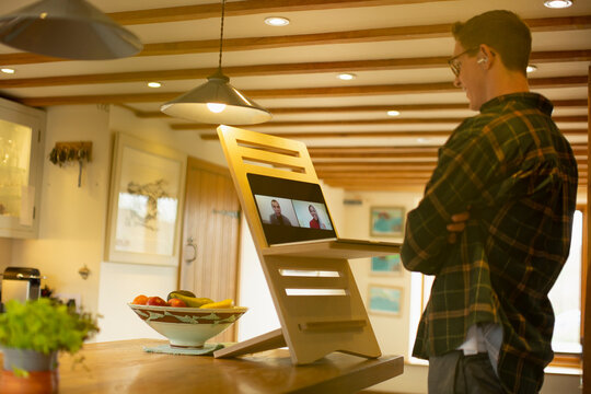 Man video conferencing with colleagues at laptop stand desk in kitchen