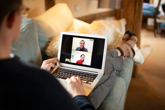 Man video conferencing with colleagues on laptop screen from sofa