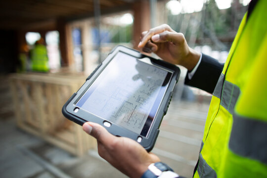 Male architect looking at blueprints on digital tablet