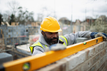 Male construction worker using level tool on brick wall