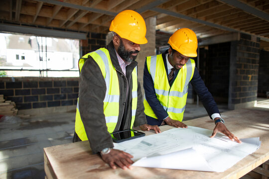 Male architect and foreman looking at blueprints at construction site